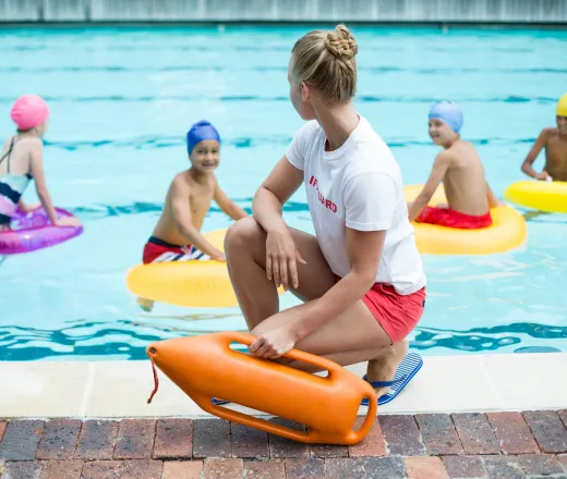 photo of lifeguard on pool deck with children in pool