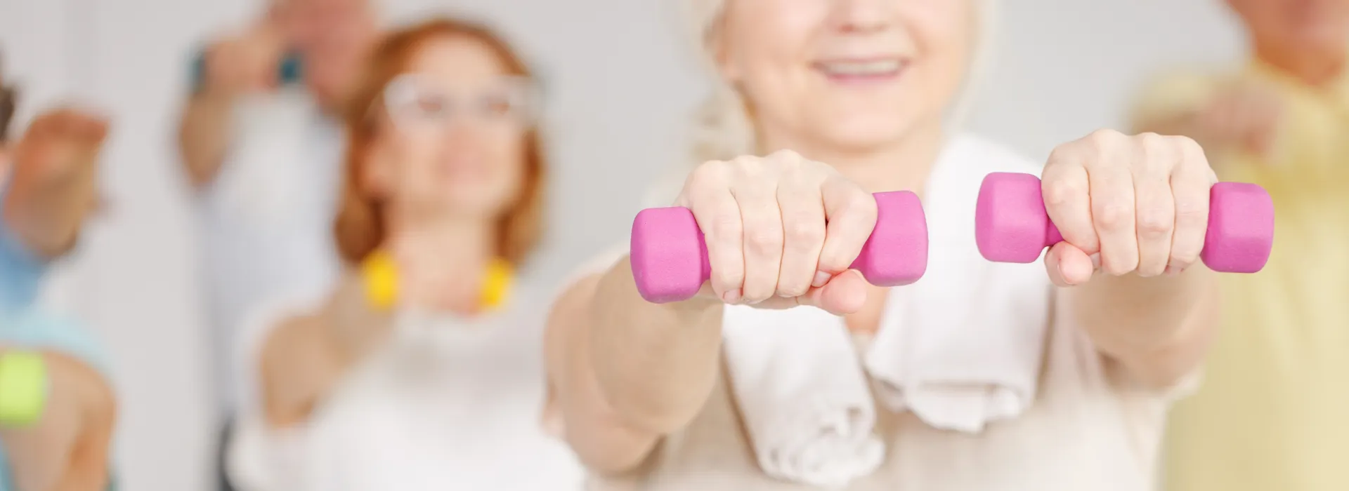close up of women with light hand weights, other seniors in background