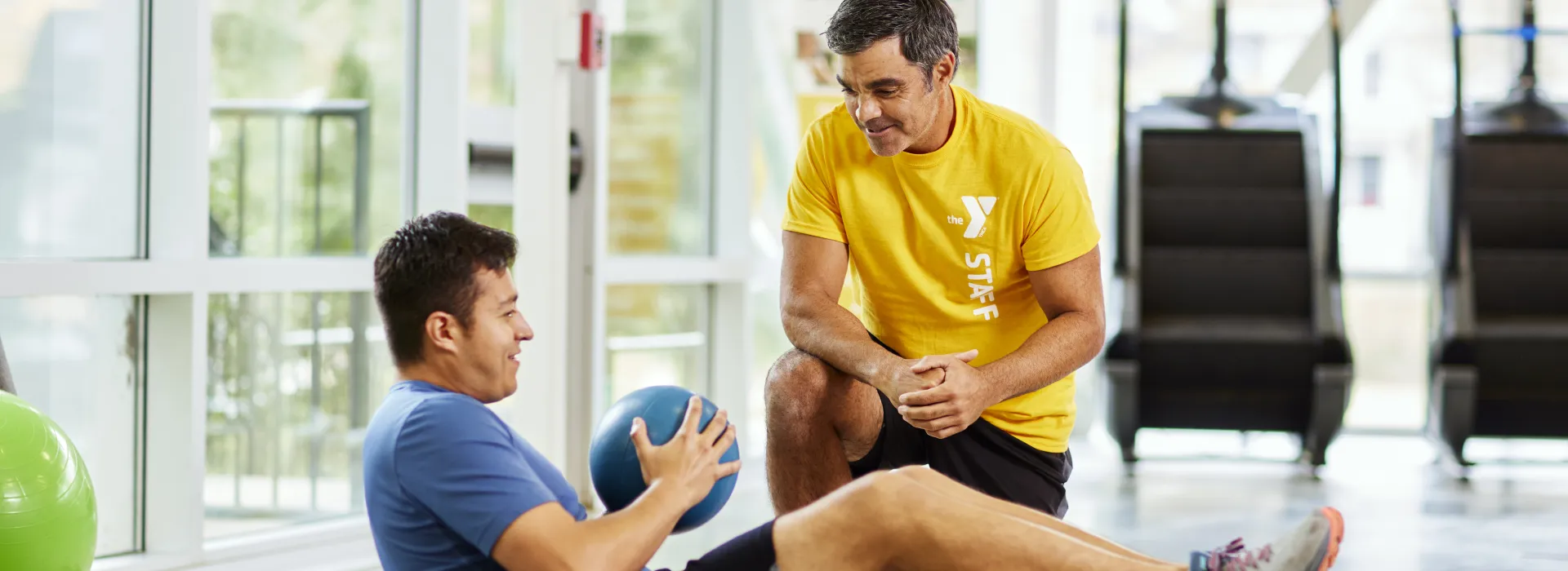 personal trainer kneeling next to man with bosu ball doing crunches